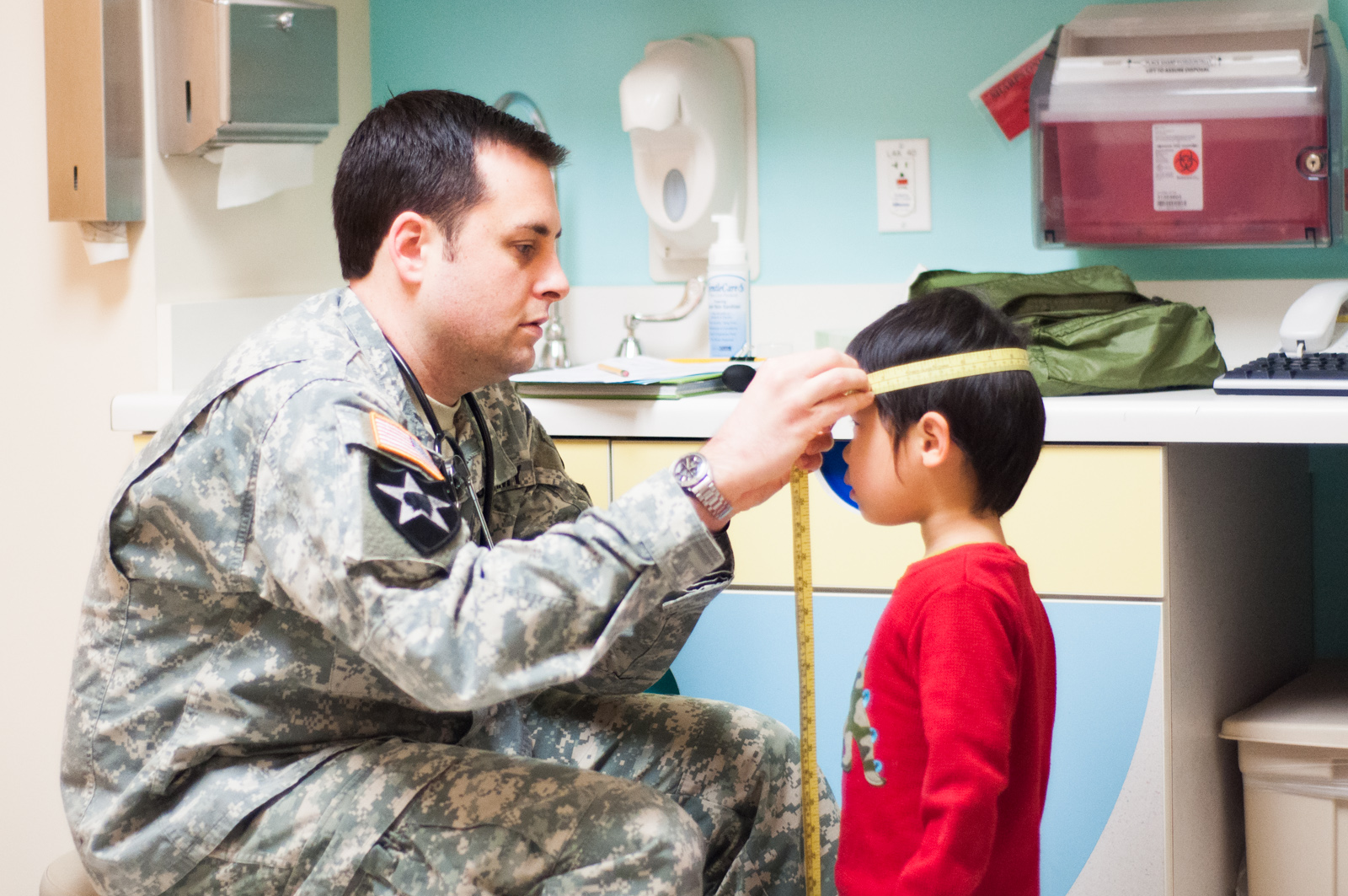 PA in military uniform performing a well child exam on a young boy